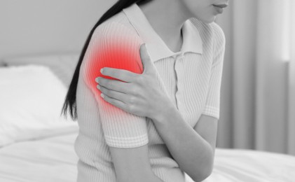 Woman suffering from pain in shoulder at home, closeup. Black and white effect