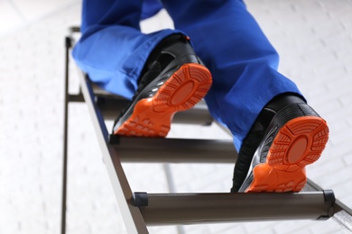Photo of Professional worker climbing up ladder indoors, low angle view