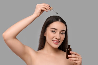 Photo of Young woman applying essential oil onto hair roots on light grey background