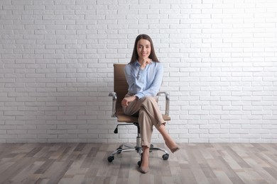 Photo of Young businesswoman sitting in office chair near white brick wall indoors