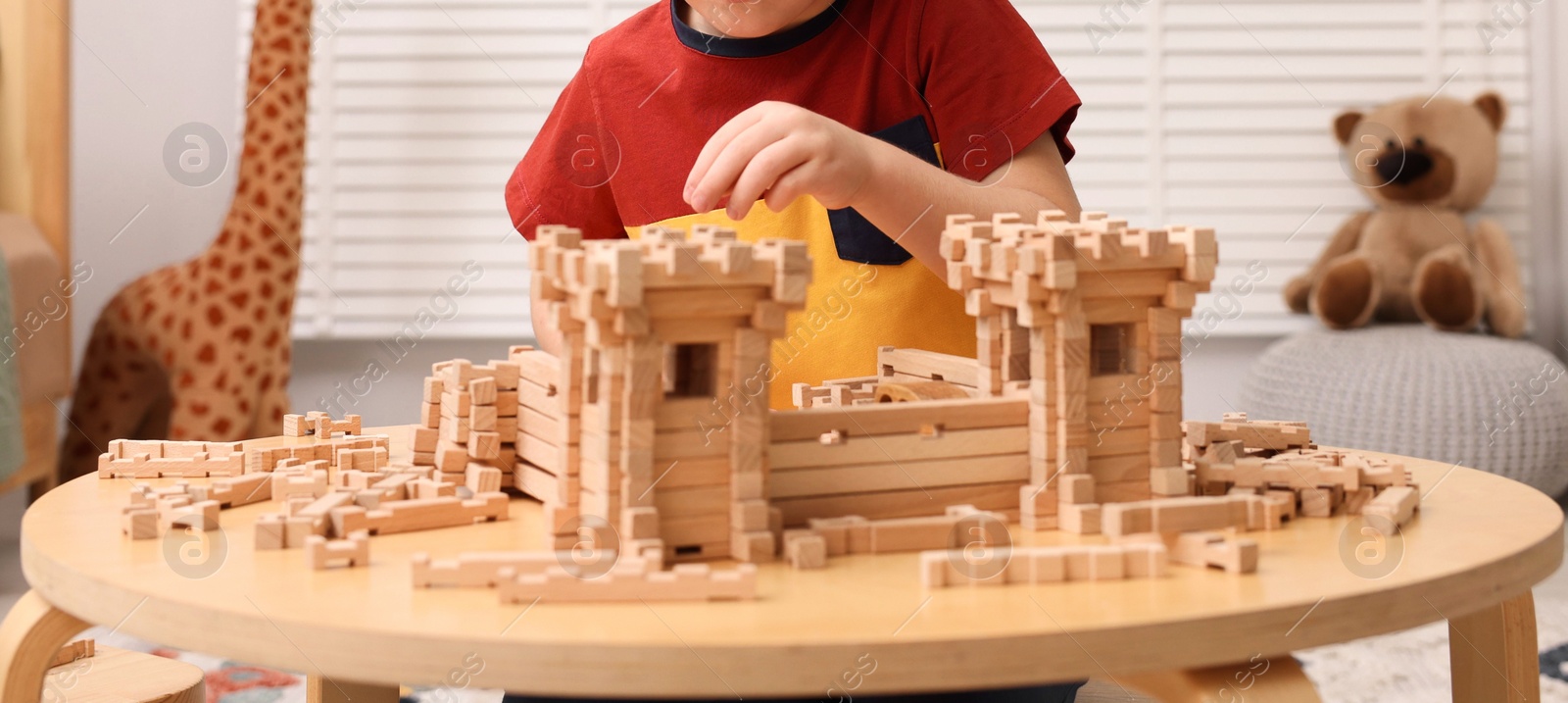 Photo of Little boy playing with wooden construction set at table in room, closeup. Child's toy