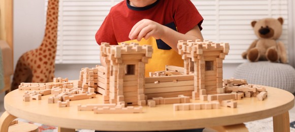 Little boy playing with wooden construction set at table in room, closeup. Child's toy