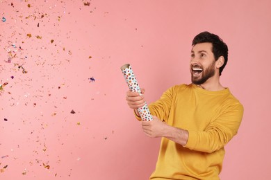 Photo of Emotional man blowing up party popper on pink background. Space for text