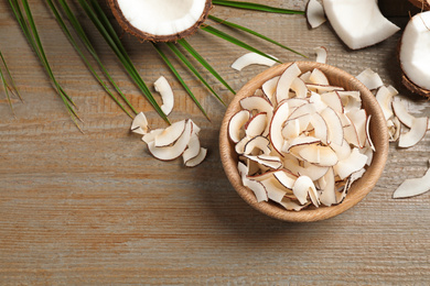 Tasty coconut chips on wooden table, flat lay. Space for text