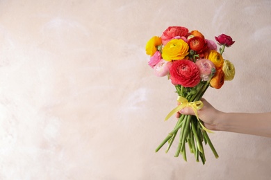 Woman holding beautiful ranunculus flowers against beige background, closeup. Space for text