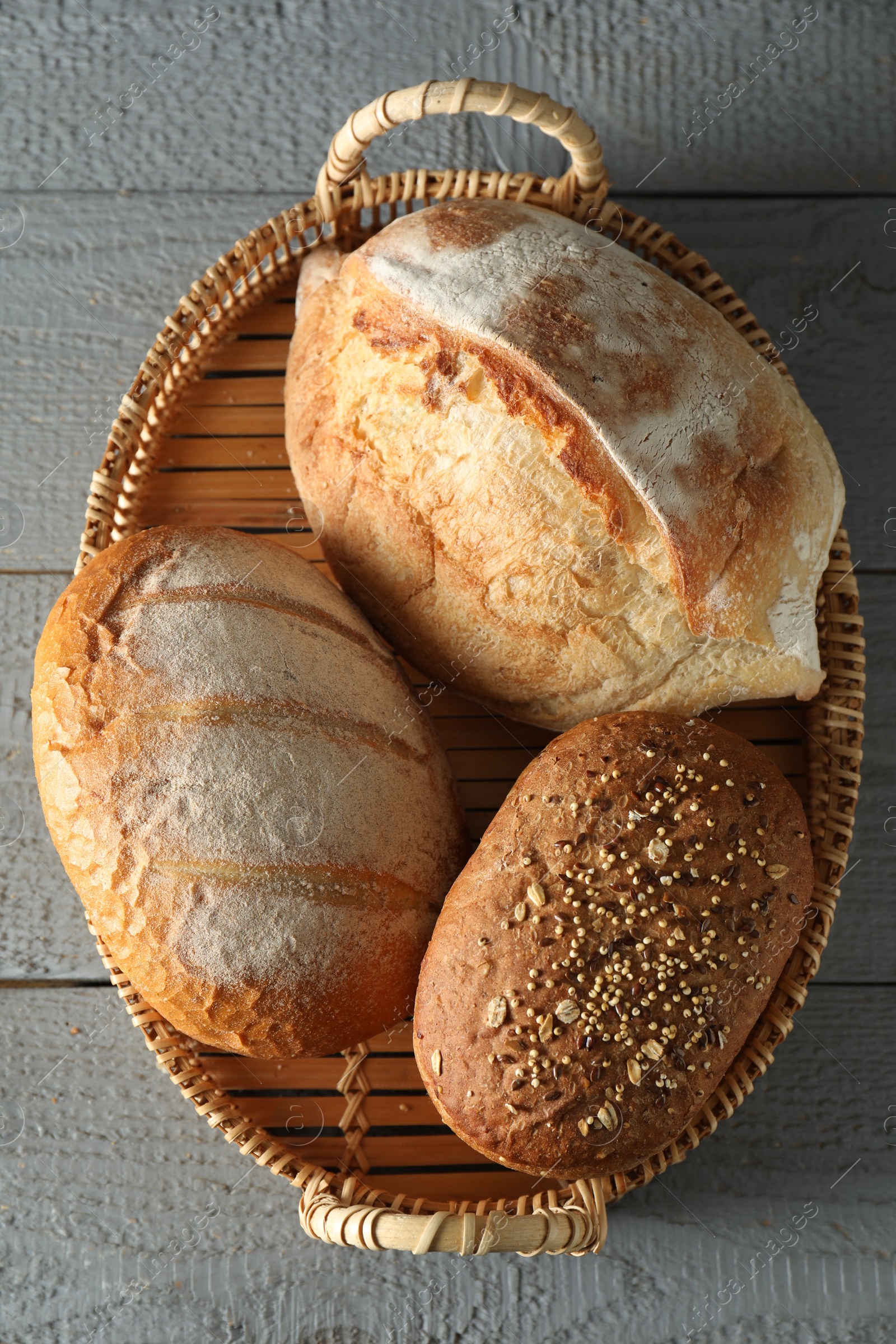 Photo of Wicker basket with different types of fresh bread on grey wooden table, top view