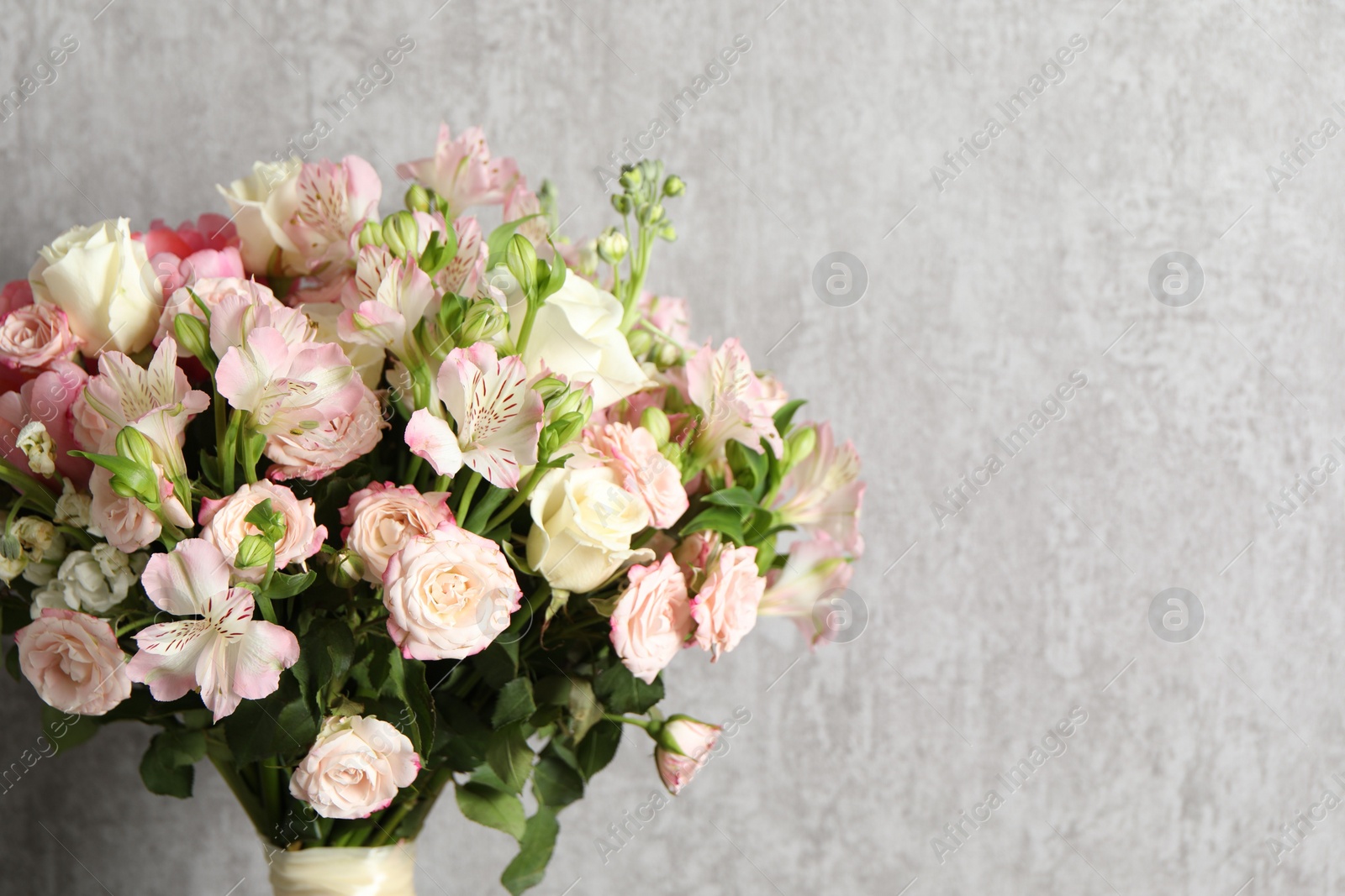 Photo of Beautiful bouquet of fresh flowers near grey wall, space for text