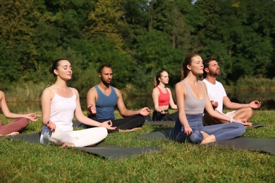 Group of people practicing yoga on mats outdoors. Lotus pose