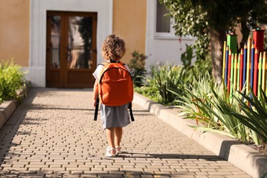 Photo of Little girl walking to kindergarten outdoors on sunny day, back view. Space for text