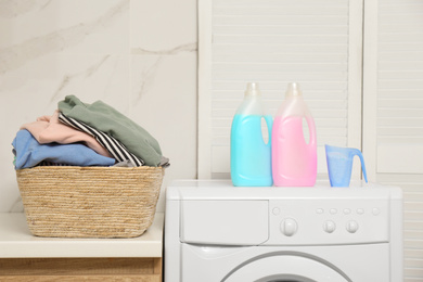 Photo of Wicker basket with laundry, detergents and washing machine in bathroom