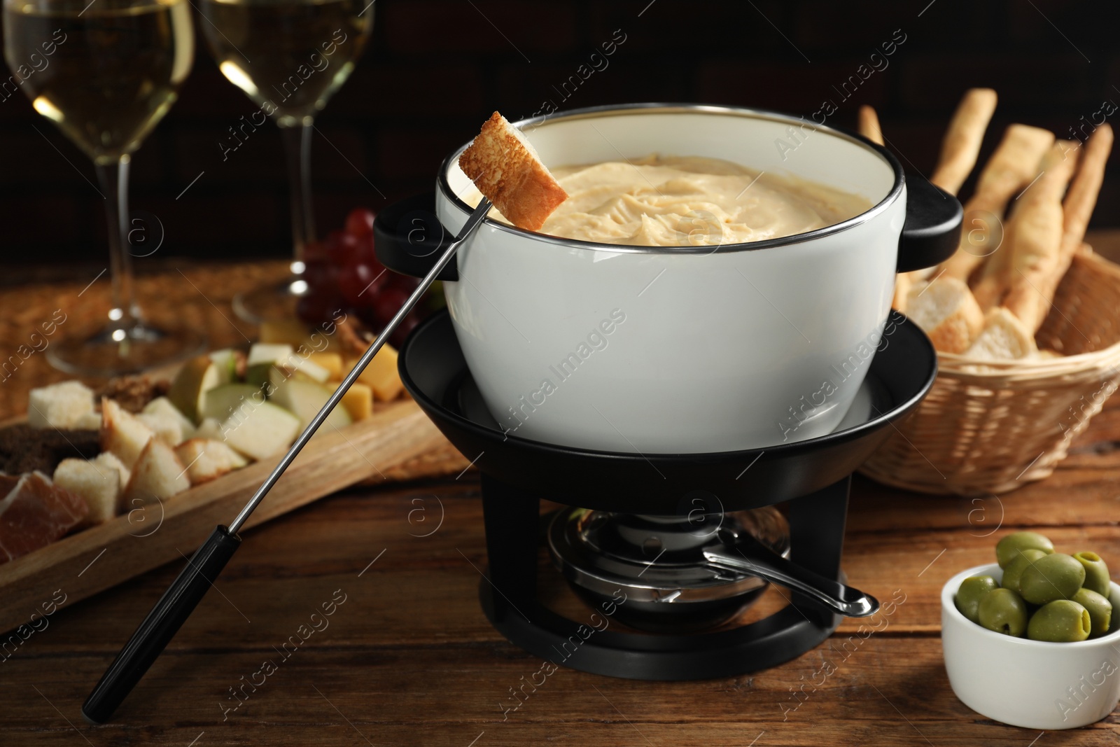 Photo of Fondue with tasty melted cheese, forks, different snacks and wine on wooden table