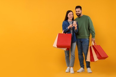 Photo of Happy couple with shopping bags and smartphone on orange background. Space for text