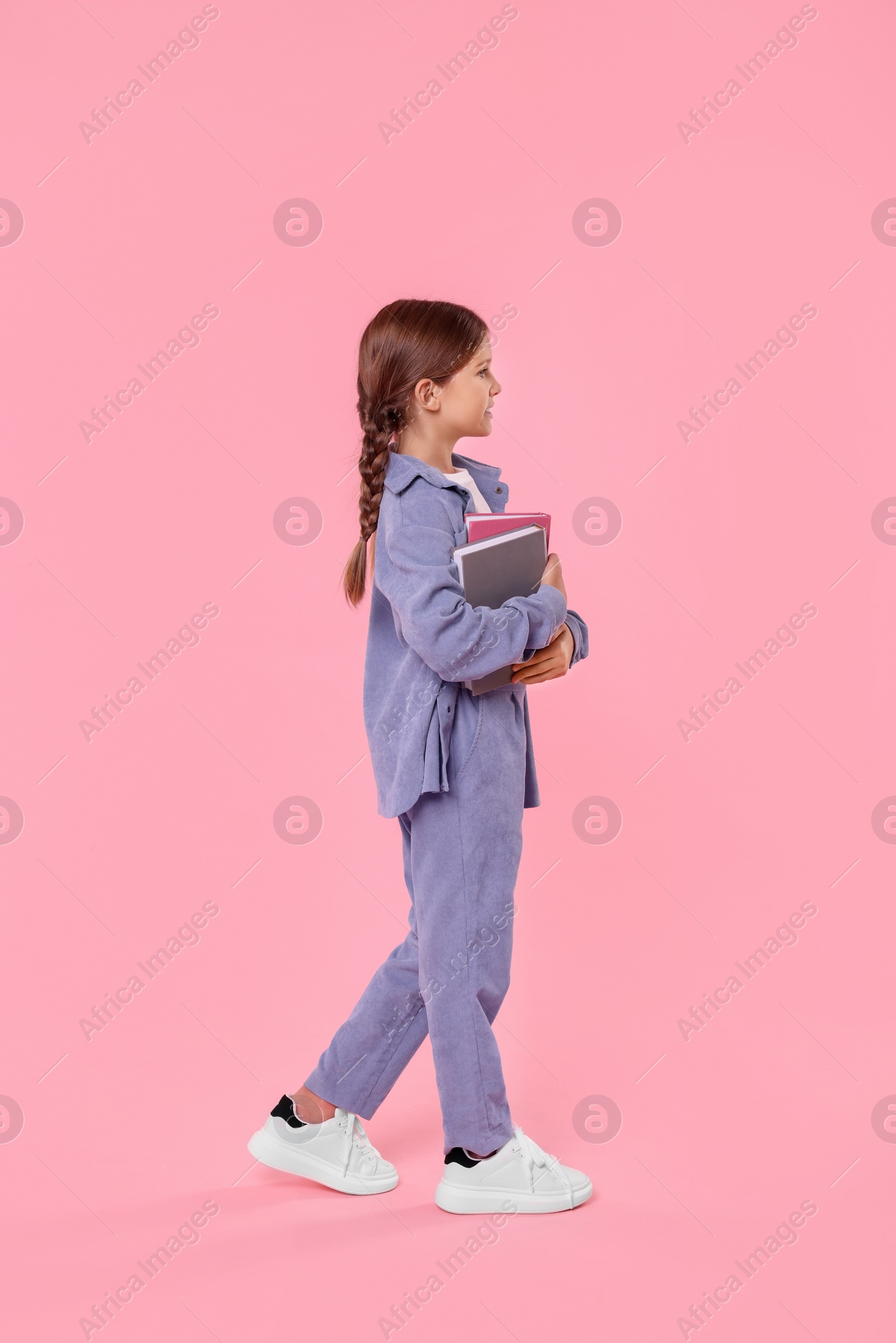 Photo of Cute schoolgirl with books on pink background