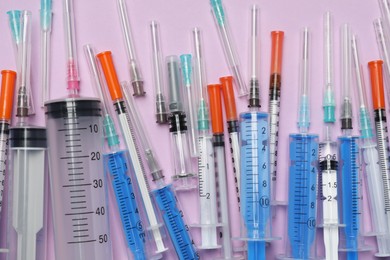 Disposable syringes with needles on violet background, flat lay