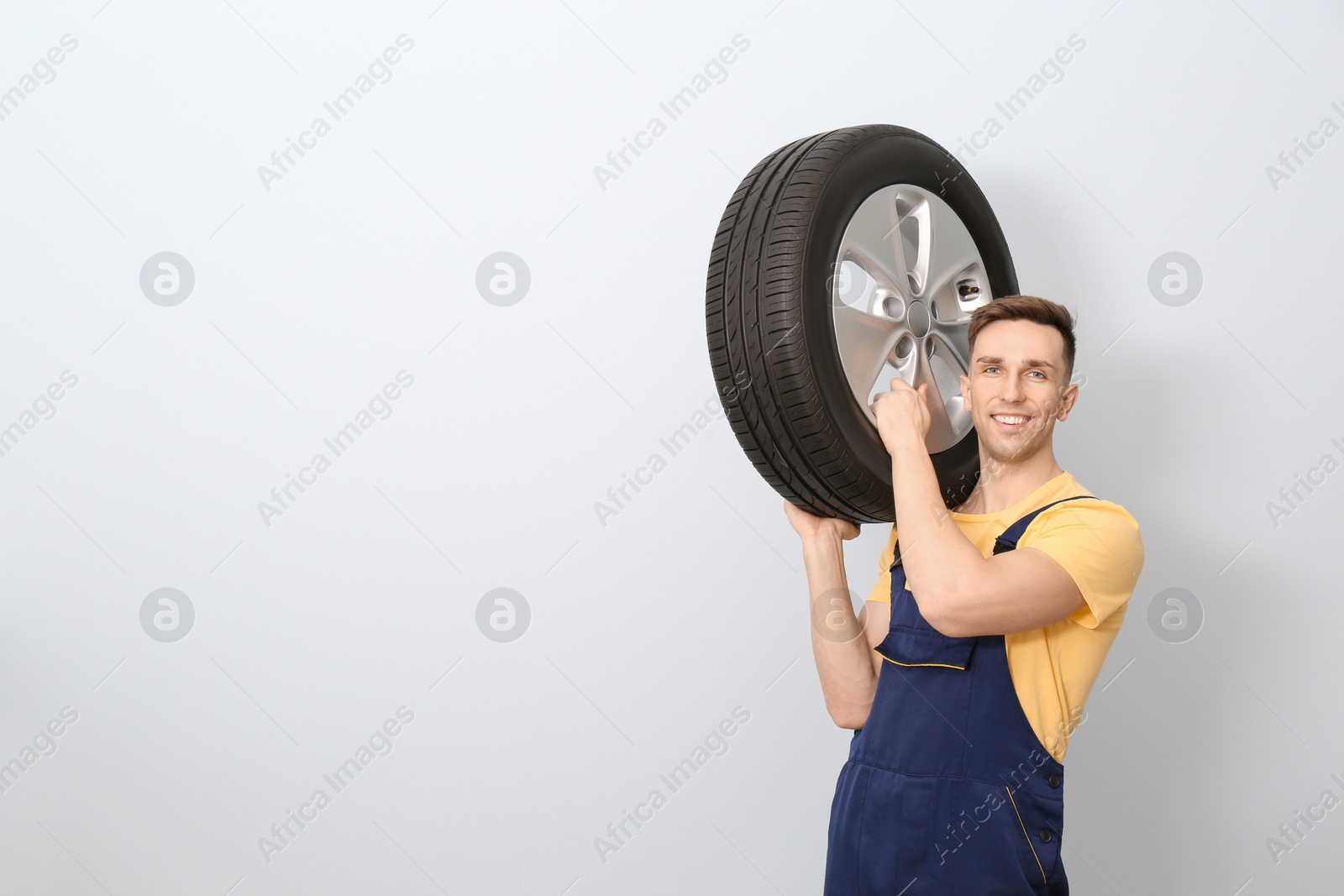 Photo of Male mechanic with car tire on light background