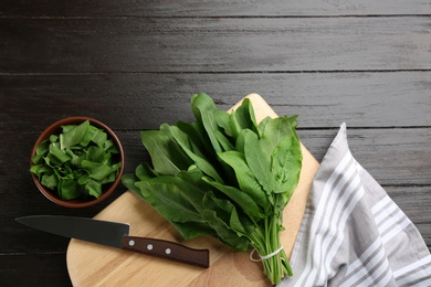 Fresh green sorrel leaves and knife on black wooden table, flat lay