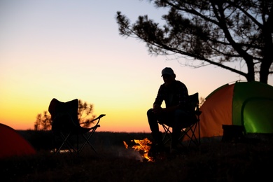 Photo of Silhouette of man near bonfire at camping in evening