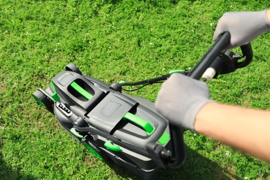 Photo of Above view of man cutting grass with lawn mower in garden on sunny day, closeup