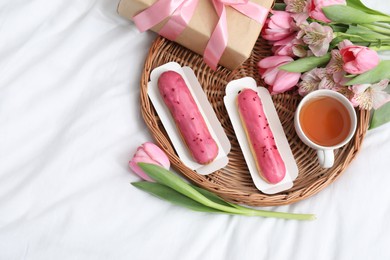 Photo of Tasty breakfast. Delicious eclairs, tea, flowers and gift box on bed, top view. Space for text