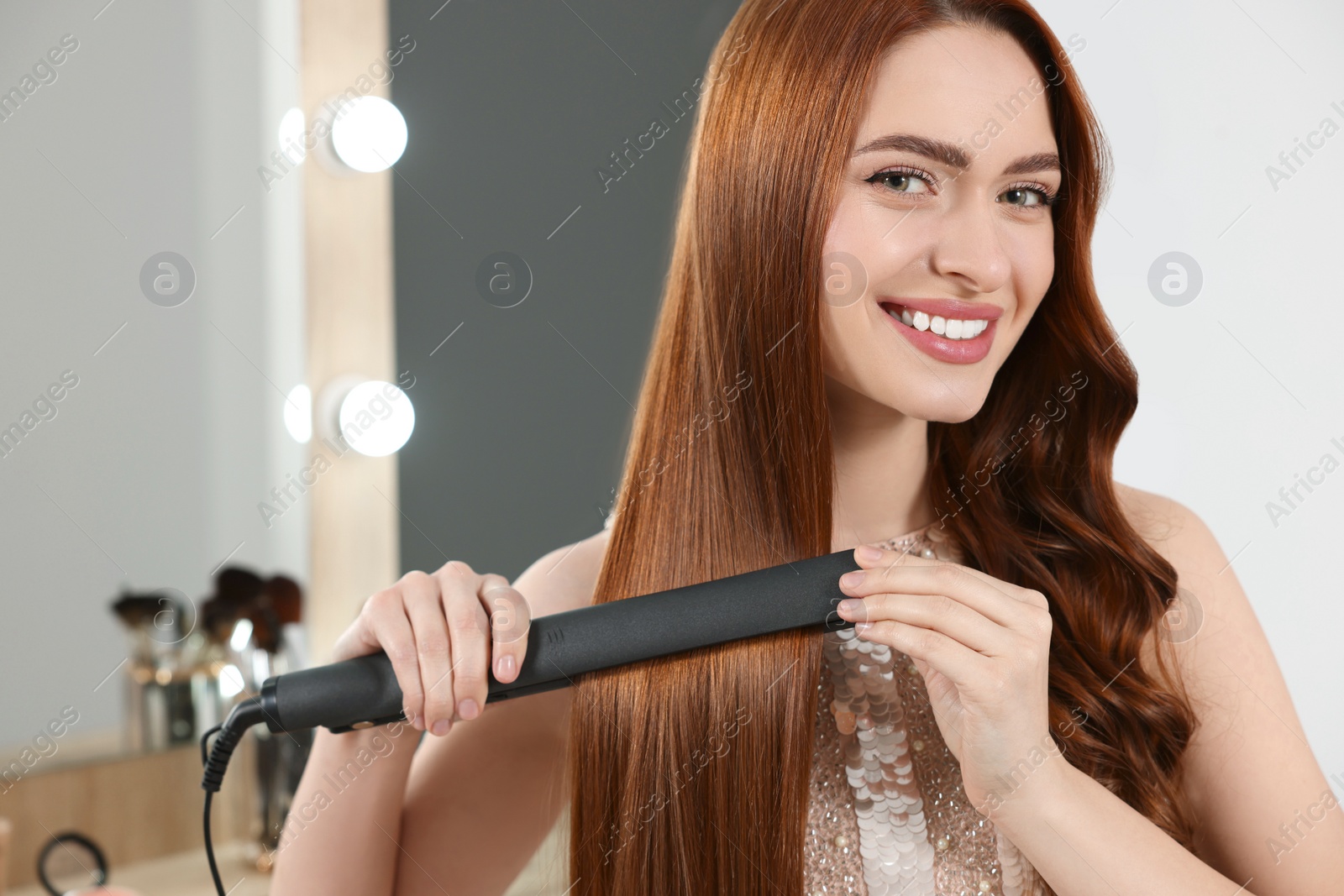 Photo of Beautiful woman using hair iron in room