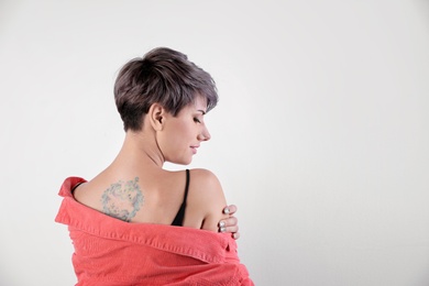 Trendy young woman with tattoo on white background. Space for text