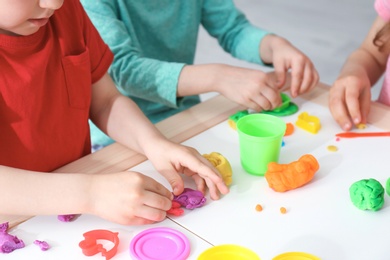 Photo of Cute little children using play dough at table, closeup