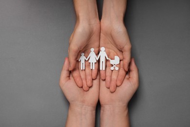 Photo of Couple holding paper family figures on grey background, top view. Insurance concept