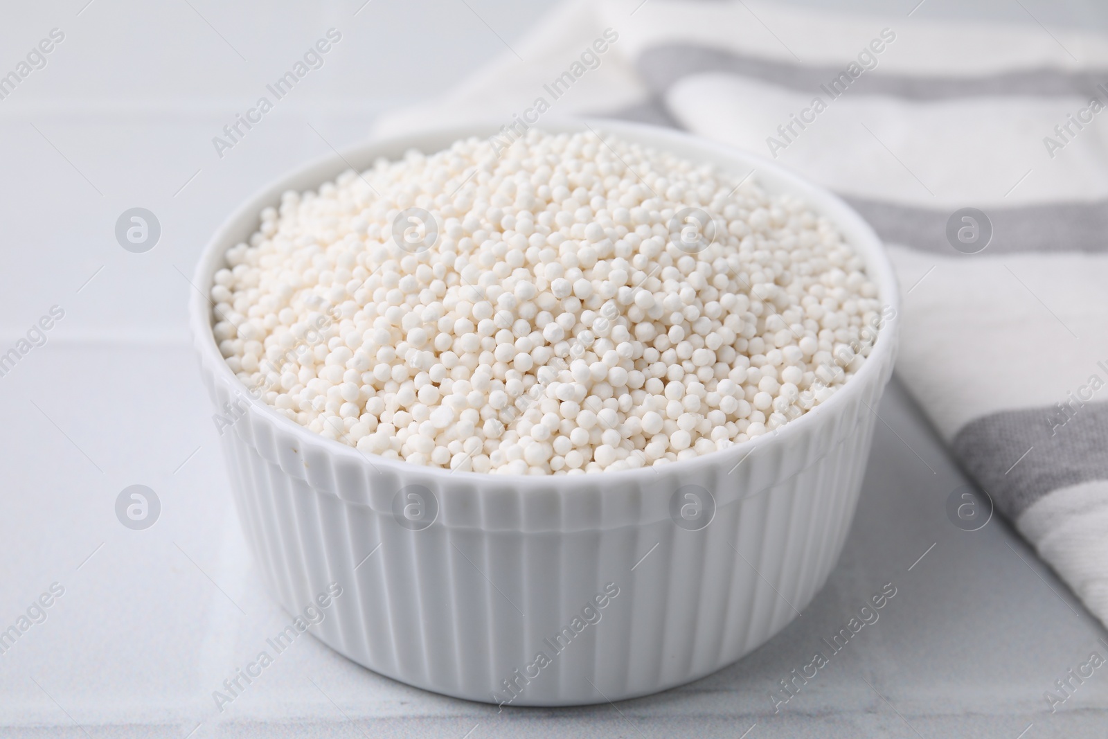 Photo of Tapioca pearls in bowl on white tiled table, closeup