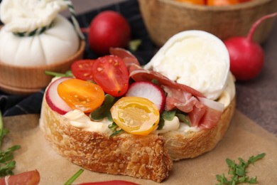 Photo of Delicious sandwich with burrata cheese, ham, radish and tomatoes on table, closeup