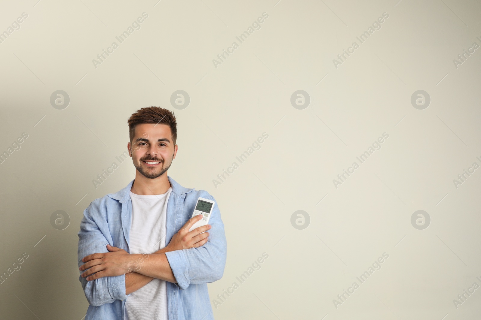 Photo of Happy young man with air conditioner remote control on beige background. Space for text
