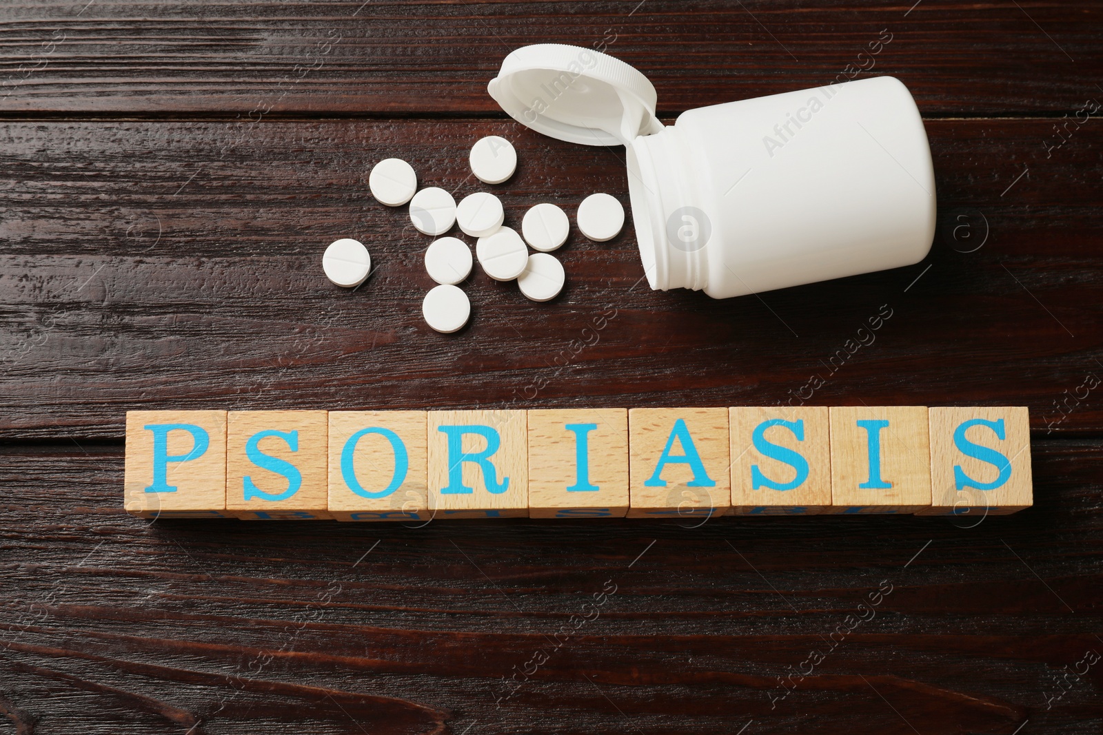 Photo of Word Psoriasis made of cubes with letters and pills on wooden table, flat lay