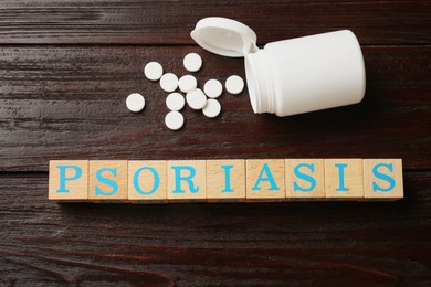 Word Psoriasis made of cubes with letters and pills on wooden table, flat lay