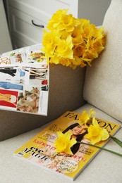 Photo of Beautiful daffodils and magazines on sofa indoors