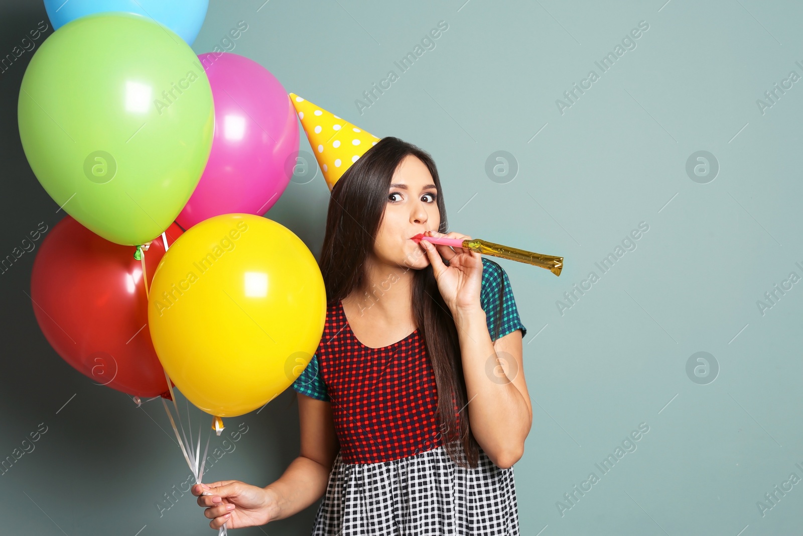 Photo of Young woman with bright balloons and party blower on color background. Birthday celebration