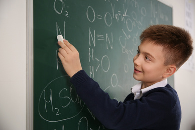Schoolboy writing chemical formulas on chalkboard in classroom