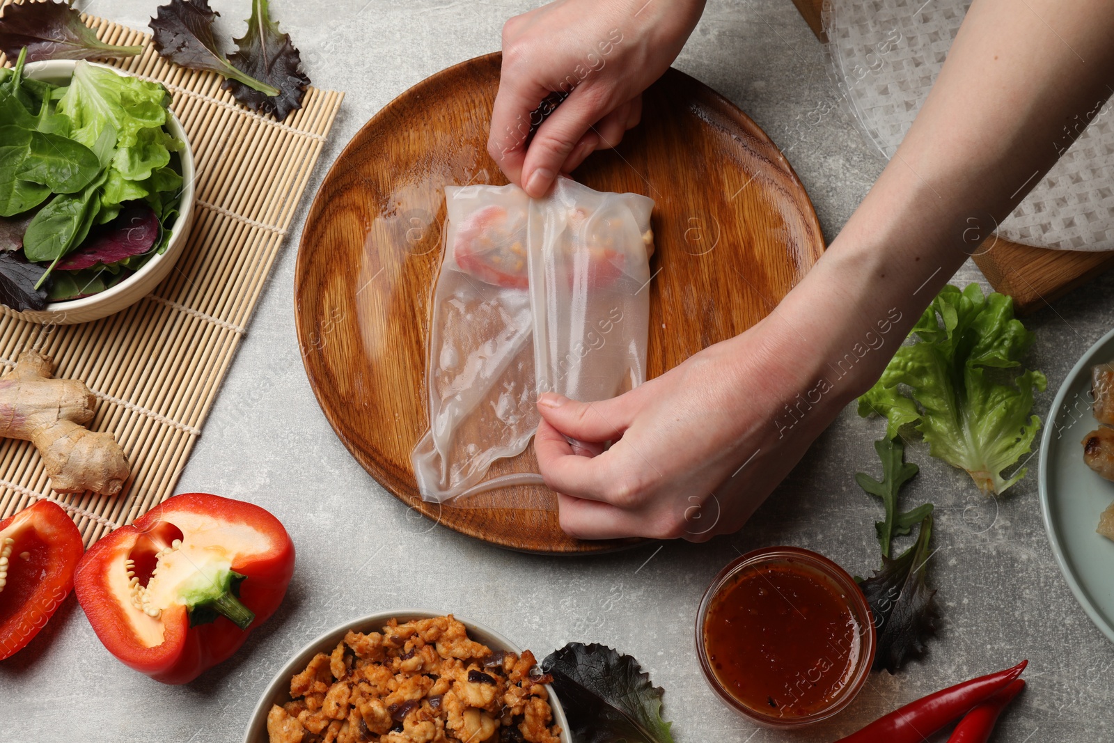 Photo of Woman making tasty spring roll at grey table, top view