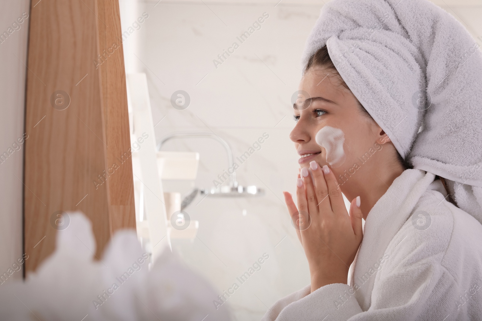 Photo of Beautiful teenage girl applying cleansing foam onto face in bathroom. Skin care cosmetic