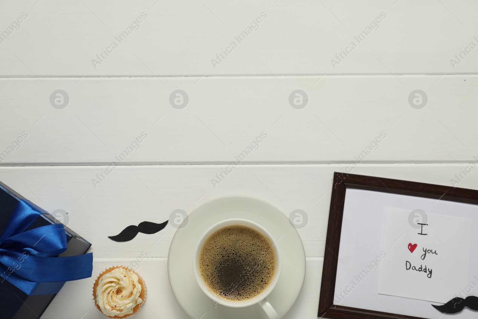 Photo of Father's day celebration. Flat lay composition of card with phrase I Love You Daddy and cup of aromatic coffee on white wooden table. Space for text