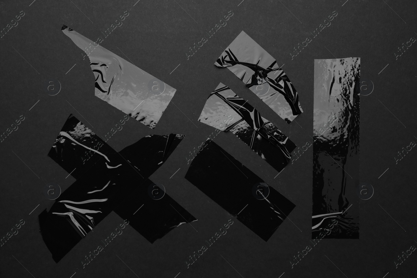 Photo of Many pieces of adhesive tape on black background, flat lay