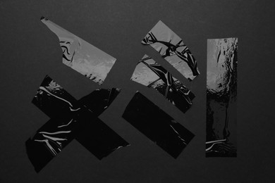 Photo of Many pieces of adhesive tape on black background, flat lay