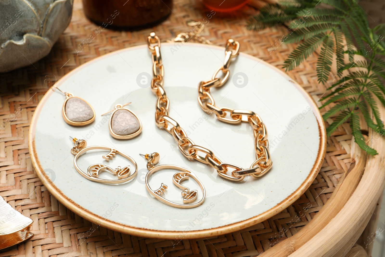 Photo of Plate with stylish golden bijouterie on wicker table, closeup