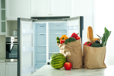 Photo of Paper bags with fresh products on table near modern refrigerator in kitchen
