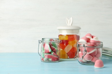Photo of Glass jars with tasty jelly candies on blue wooden table against white background, space for text