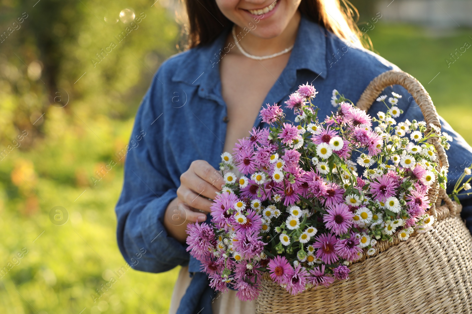 Photo of Woman holding wicker basket with beautiful wild flowers outdoors, closeup