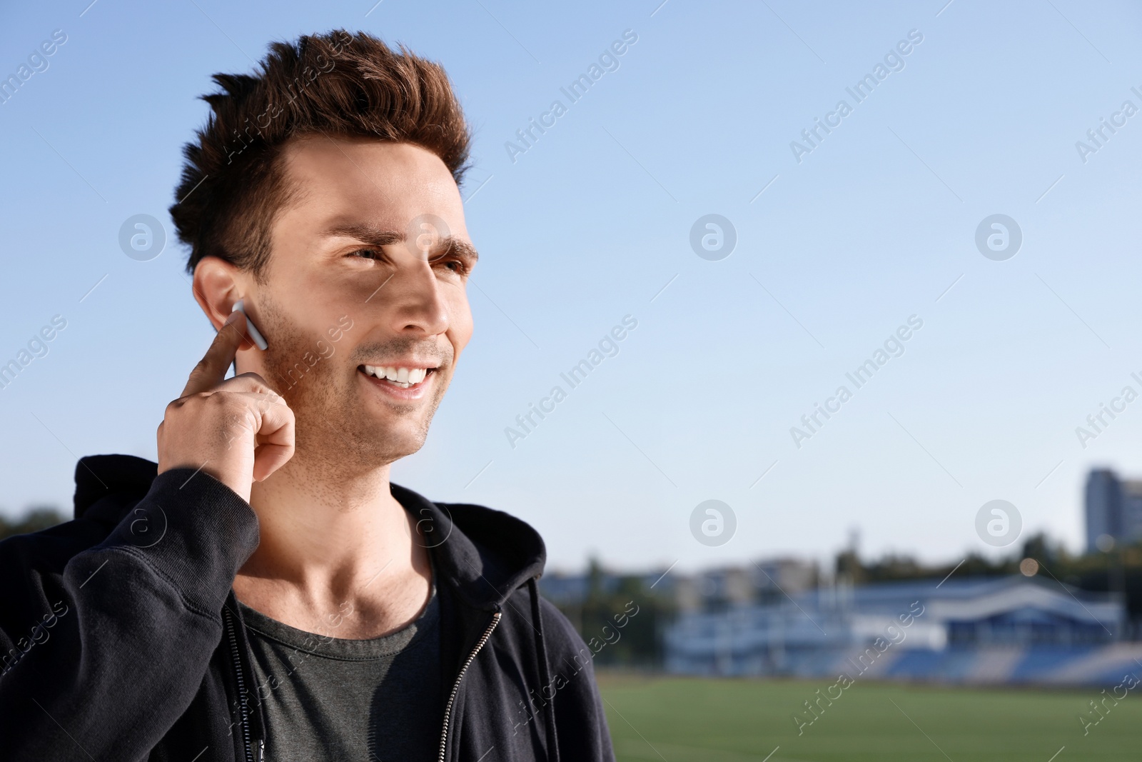 Photo of Young sportsman with wireless earphones at stadium