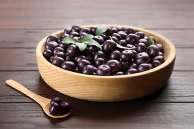 Photo of Tasty acai berries in bowl and spoon on wooden table, closeup