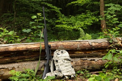 Hunting rifle and backpack near fallen tree in forest