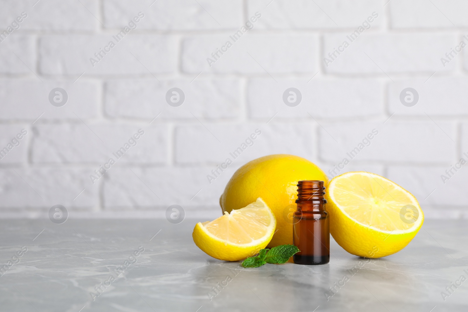 Photo of Bottle of essential oil with lemons and mint on grey marble table against white brick wall. Space for text