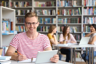 Photo of Young man studying with tablet at table in library. Space for text