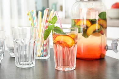 Photo of Peach cocktail in glass and jar with tap on table. Refreshing drink